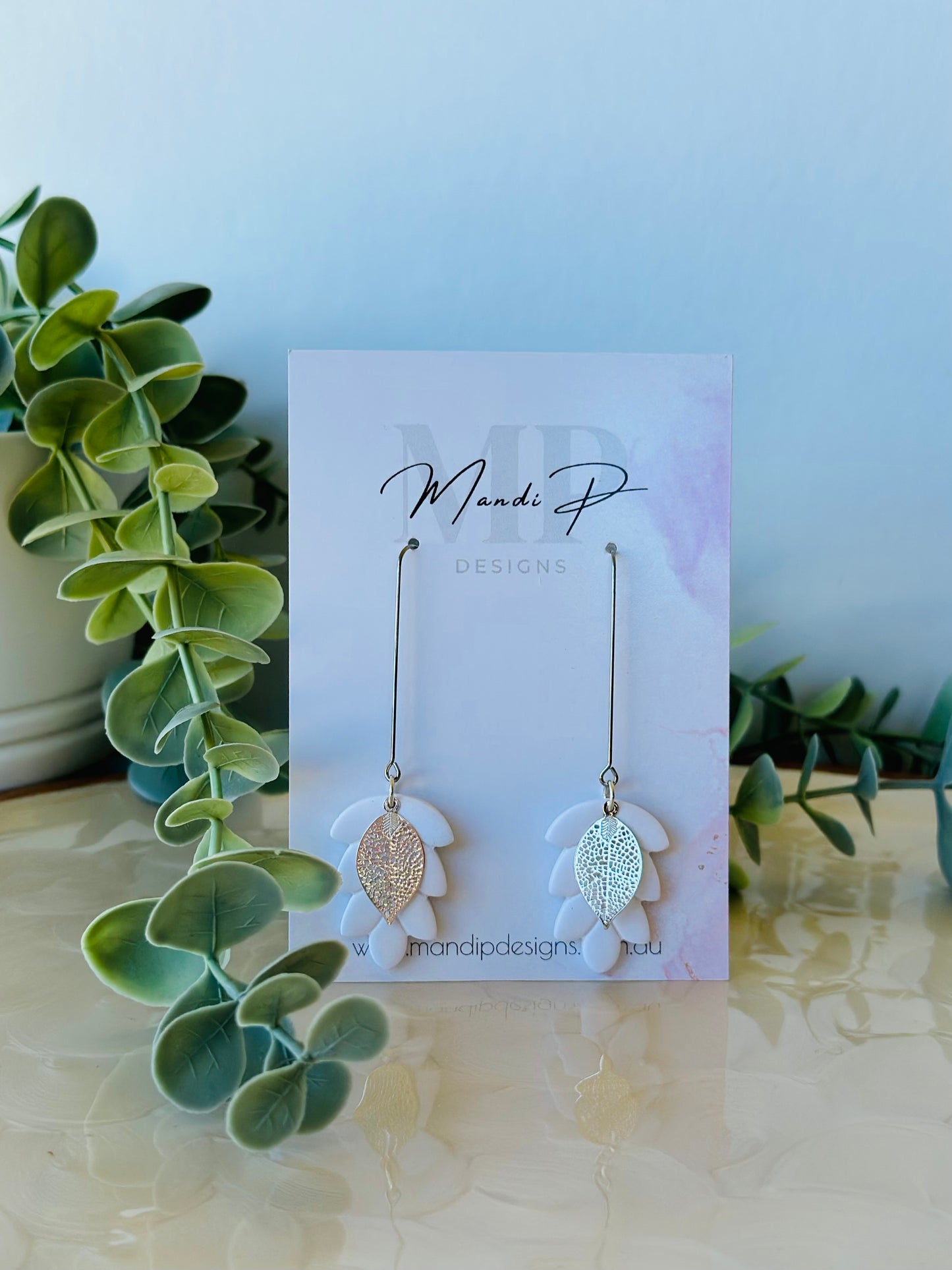 Handmade white polymer clay dangle earrings with silver metal leaf overlay and long drop surgical steel hooks – displayed on Mandi P Designs card