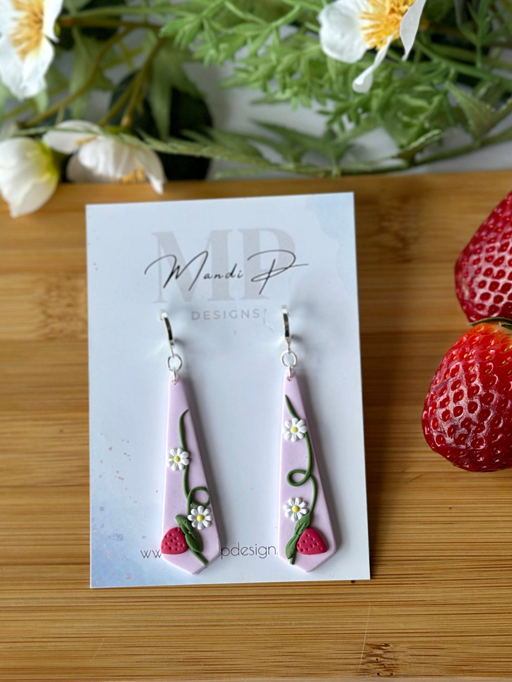 Pink earrings on a card with strawberries and flowers on a wooden board