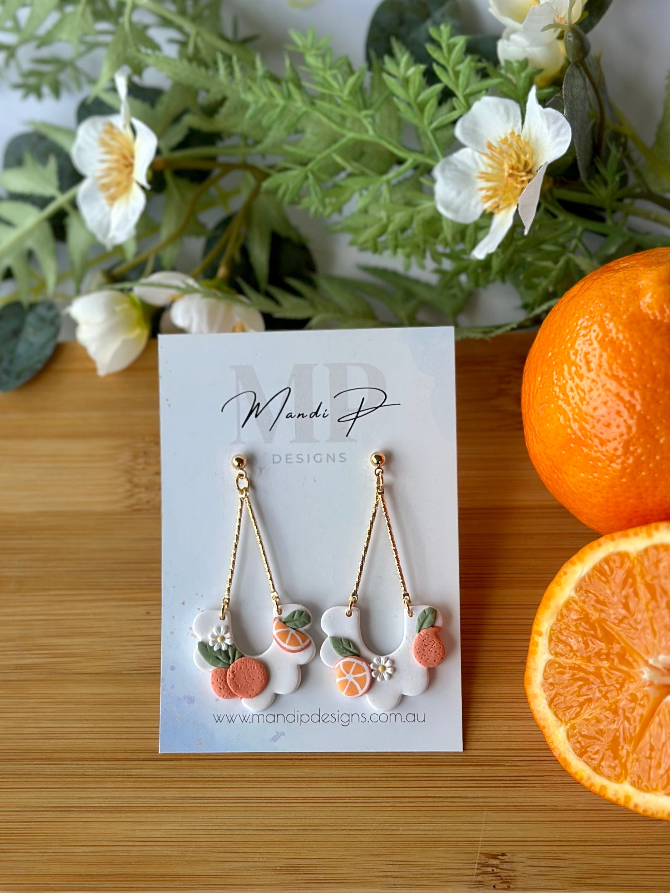 Earring set on a card with oranges and greenery on a wooden board