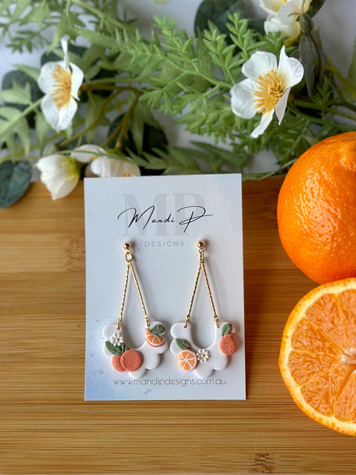 Earring set on a card with oranges and greenery on a wooden board
