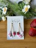 Earrings on a card with strawberries and greenery on a wooden board