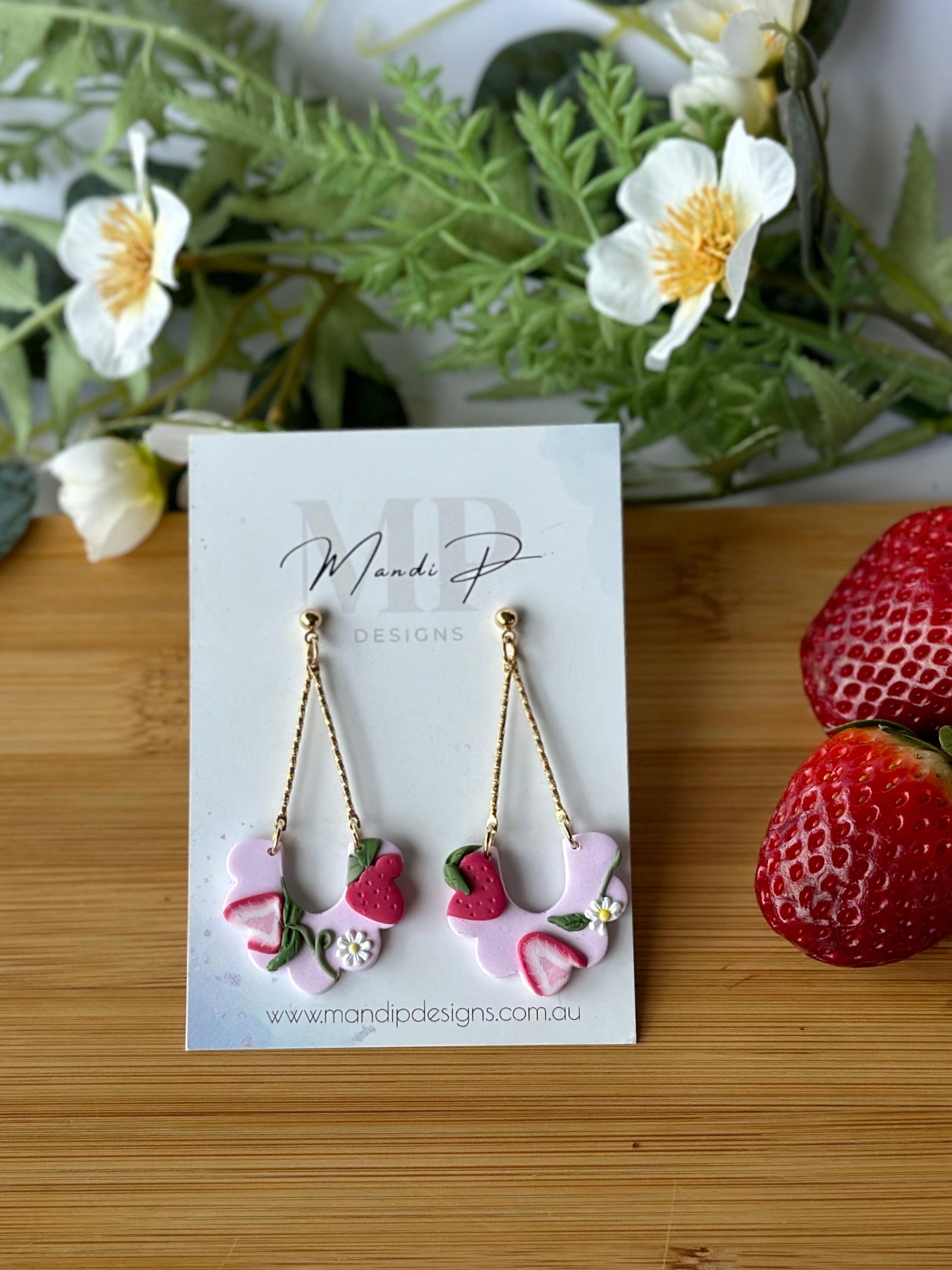 Earrings on a card with strawberries and greenery on a wooden board