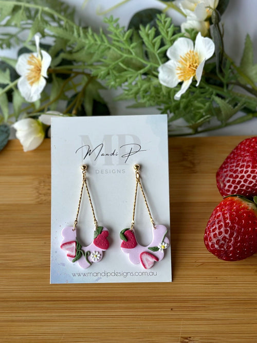 Earrings on a card with strawberries and greenery on a wooden board