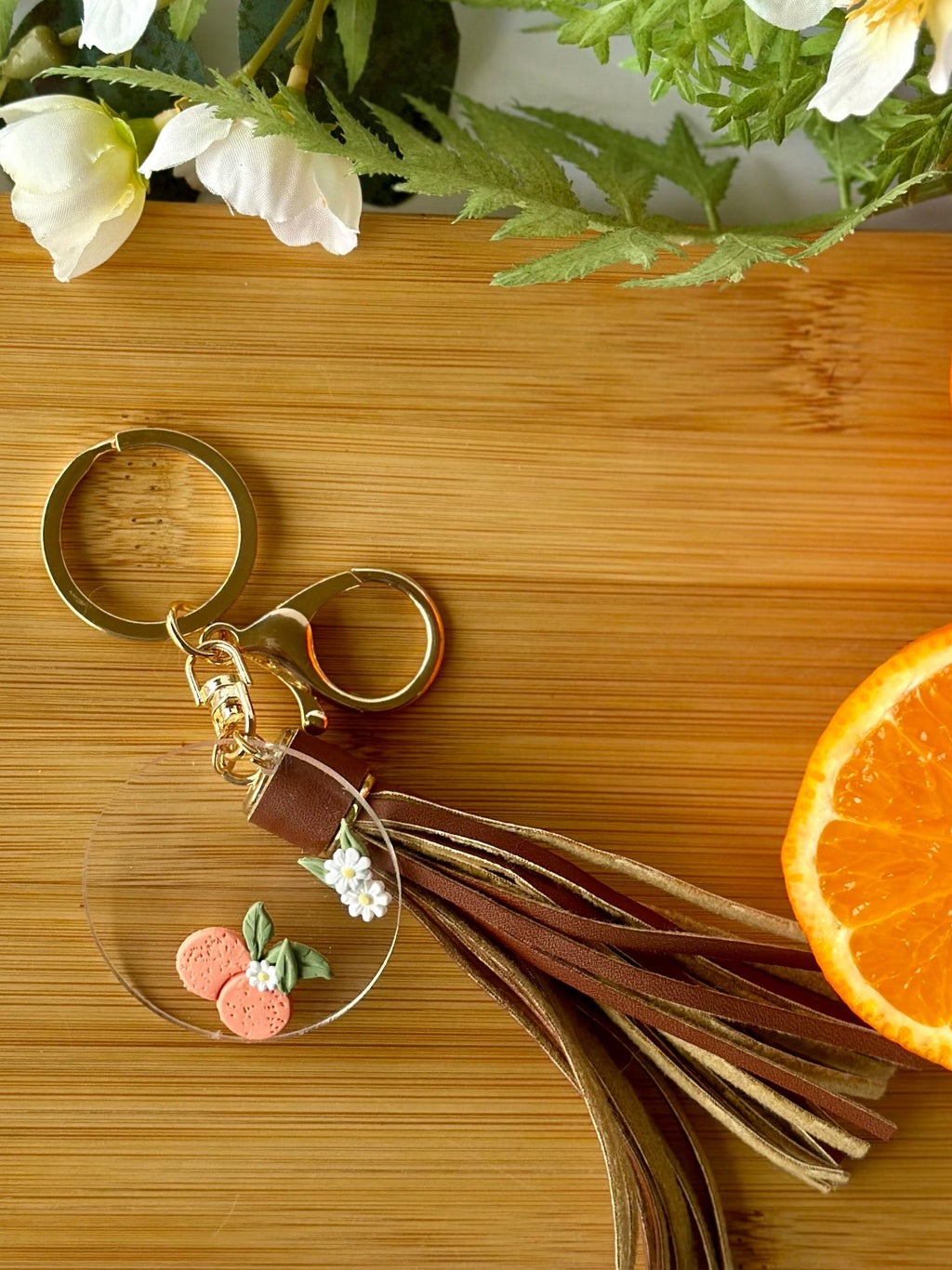 Gold keychain with tassel on a wooden surface with oranges and flowers
