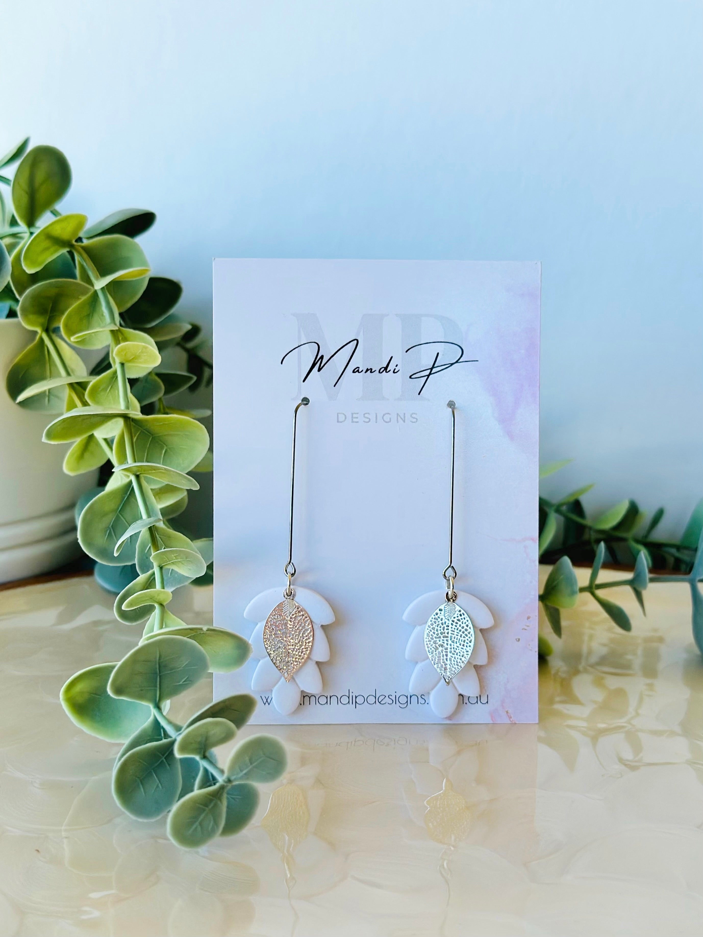 Handmade white polymer clay dangle earrings with silver metal leaf overlay and long drop surgical steel hooks – displayed on Mandi P Designs card