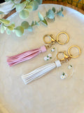 Handmade yellow and white daisy keyrings with white and pink vegan leather tassels on gold hardware – polymer clay floral charms on acrylic discs
