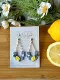 Pair of earrings on a card with lemons and greenery on a wooden board