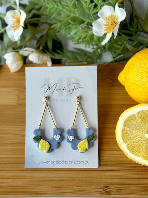 Pair of earrings on a card with lemons and greenery on a wooden board